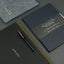 Dark gray notebook with gold text and a pen on a matching surface
