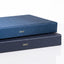 Two hardcover books stacked on a white reflective surface, with the top book in dark blue and the bottom book in dark navy, both printed with '2027' in gold on the front spines.