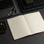 Open notebook on a dark surface with a laptop and cards in the background