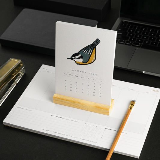Calendar with a bird illustration on a desk with a laptop and office supplies.